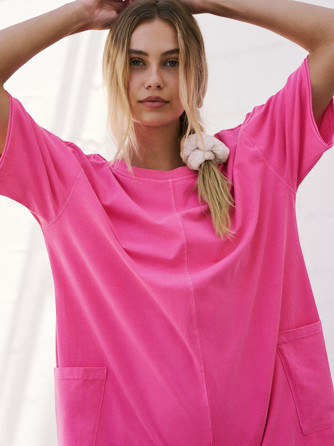 URH Imani Easy Jumpsuit in bright pink cotton with short sleeves and front pockets. Model has blonde hair in a ponytail.
