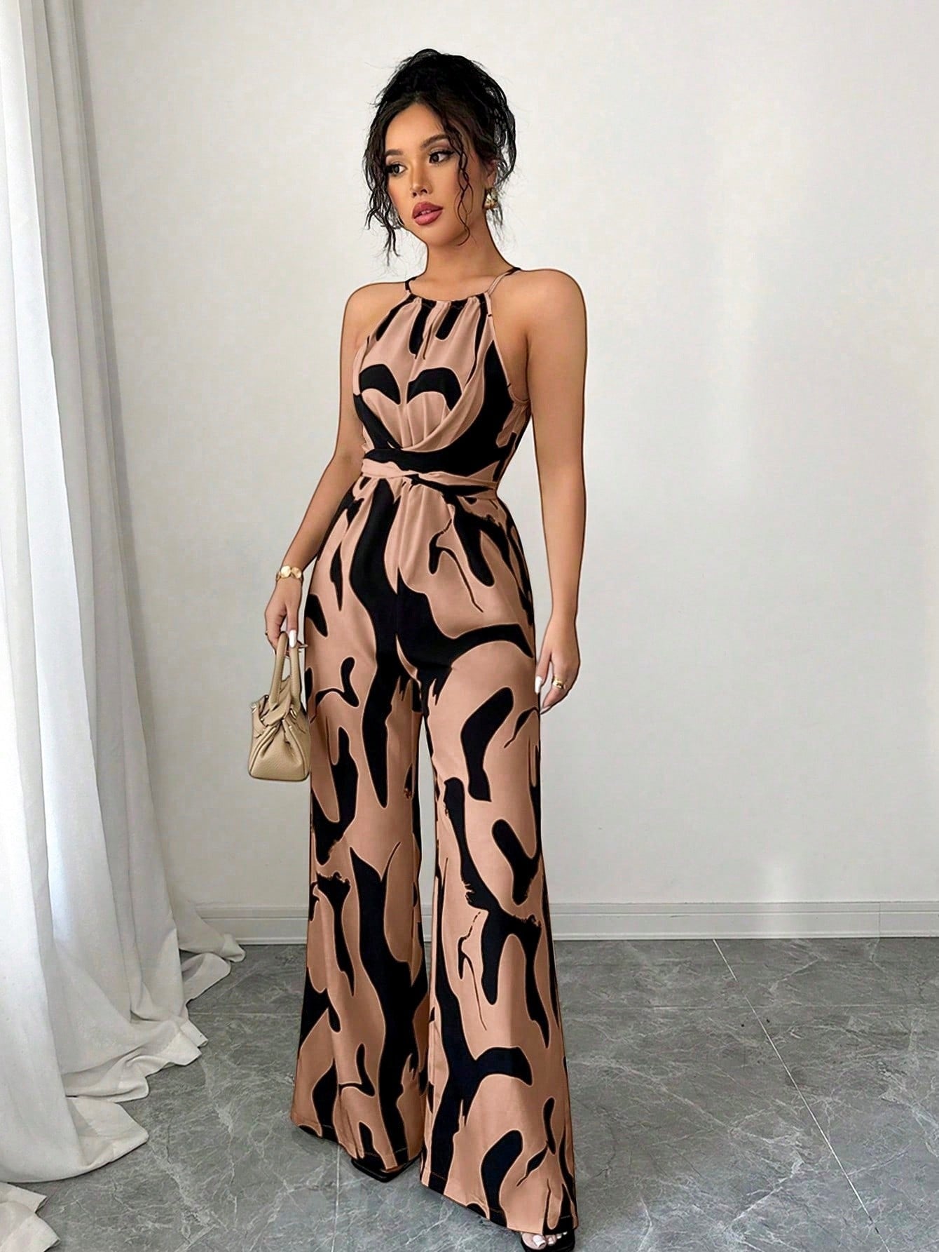 URHER Nia Utility Jumpsuit in tan with black abstract print, featuring a halter neck, wide legs, and a belted waist.
