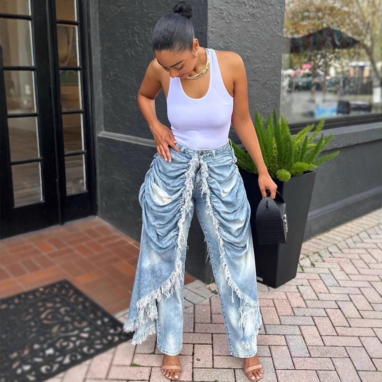 URHERHere light blue denim jeans with high-rise waist, ruched detailing, and frayed hem. Model wears white tank top and sandals.